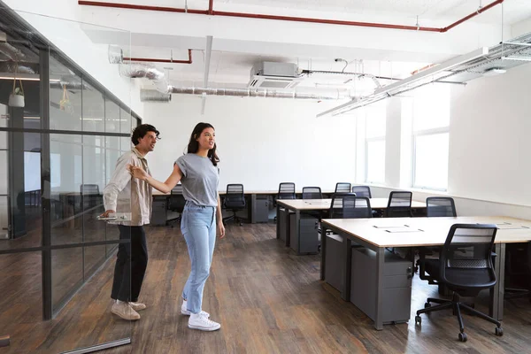 Casually dressed young man and woman looking for premises to rent for start up business walking into empty modern open plan office