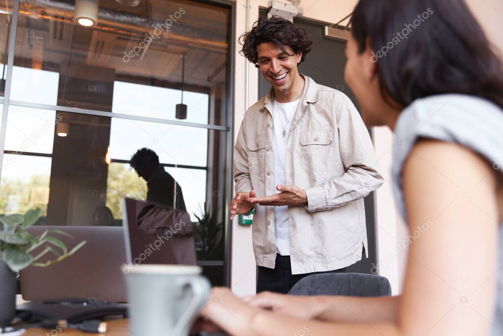 Casually dressed young man and woman working on laptops at desks preparing for online meeting in modern open plan office