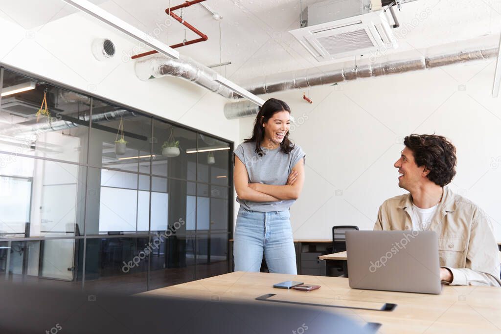 Casually dressed young man and woman working in modern open plan office standing by desk and flirting