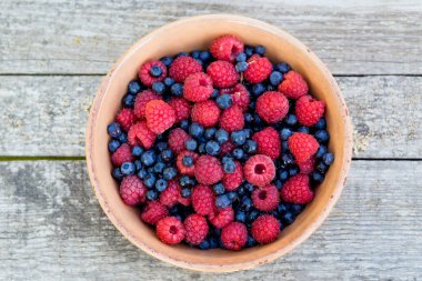 ahşap masa üzerinde yaban mersini ve ahududu kase