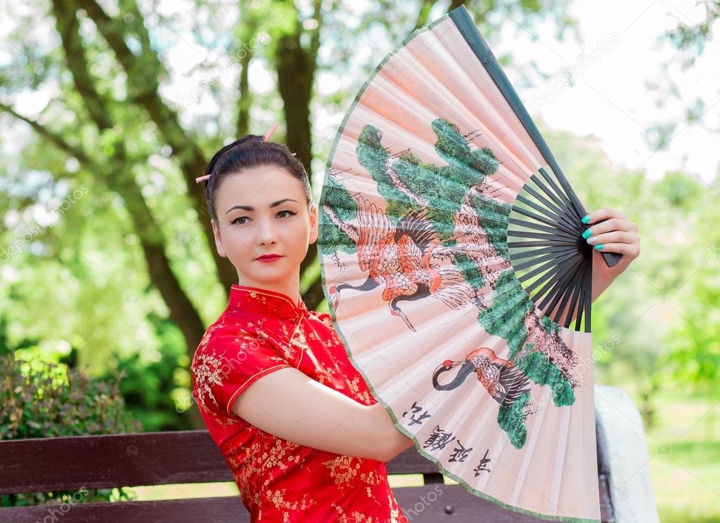 young Asian girl walking in national dress with a fan in the par