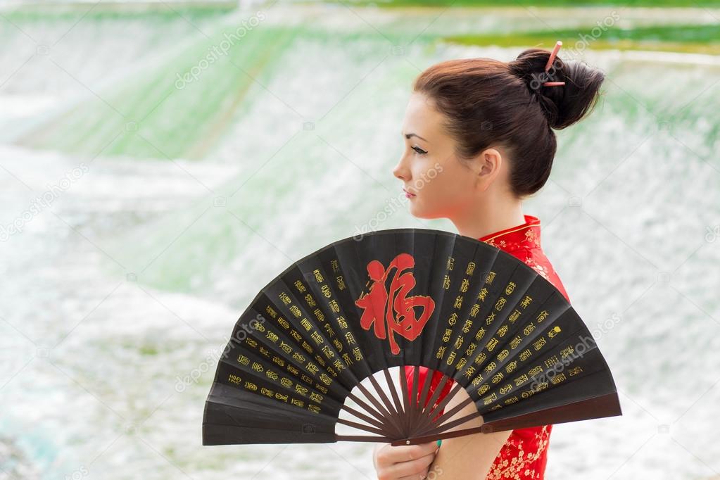 young Asian girl walking in national dress with a fan near the r