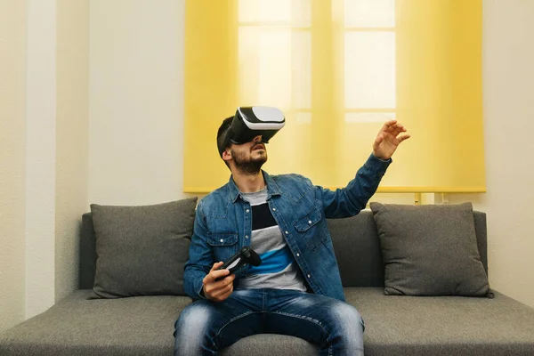 Excited man playing virtual reality games with vr glasses indoors, on yellow background.