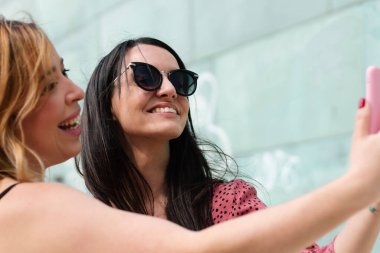 Yazlık elbiseli iki neşeli kız dışarıda selfie çekiyorlar.