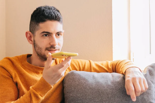 Mid adult man in yellow clothes on gray background from home, sending a voice message from his smart phone.Technology concept and voice notes