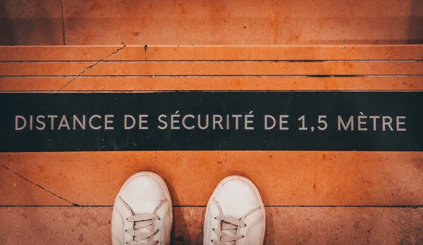 French inscription: Safe distance 1.5 meters and white sneakers on the subway stairs, top view close-up.