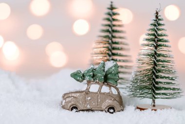Araba ve sağdaki karda iki Noel ağacı arka planda bokeh ışıkları ve soldaki yazı için yeri olan yakın plan yan görüş..