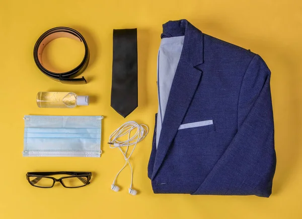 Jacket, tie, headphones, disinfector, belt, glasses, headphones and a medical mask on a yellow background, close-up top view.