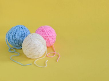 Solda üç renkli yün yumağı var. Sarı bir arkaplanda, sağda yazı için yer var. Yan görünüş yakın plan..
