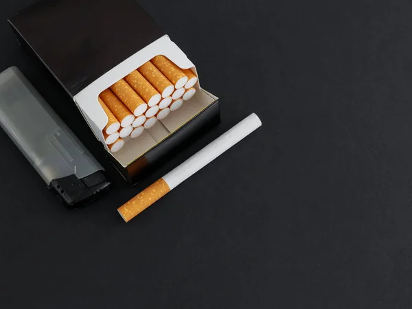 左边是一包香烟和一个打火机 旁边是一个黑色的背景 右边是一个文字位置 一个特写的顶部视图 — 图库照片