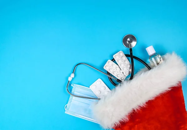 stock image Tablets, stethoscope, disinfectant and a medical mask wearing a santa claus hat on the right against a blue background and with space for text on the left, top view.