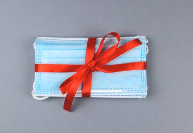 Sağlık maskeleri kırmızı kurdeleyle bağlanmış gri bir arka planda, üstten yakın plan.