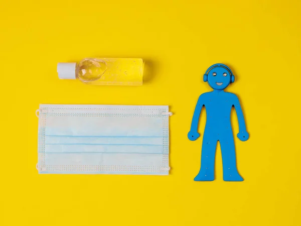 A blue man, a medical mask and a disinfectant lie in the middle on a yellow background, a close-up top view.