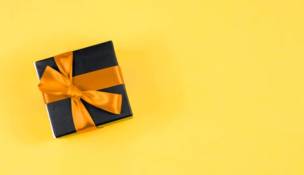 Ein Schwarzes Geschenk Mit Schleife Liegt Links Auf Gelbem Hintergrund — Stockfoto