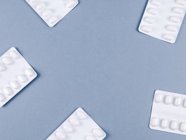 Paketlerdeki haplar gri bir arkaplanda çerçeveye yerleştirilip orta, üst görünüm ve yakın çekim için bir yere yerleştiriliyor..