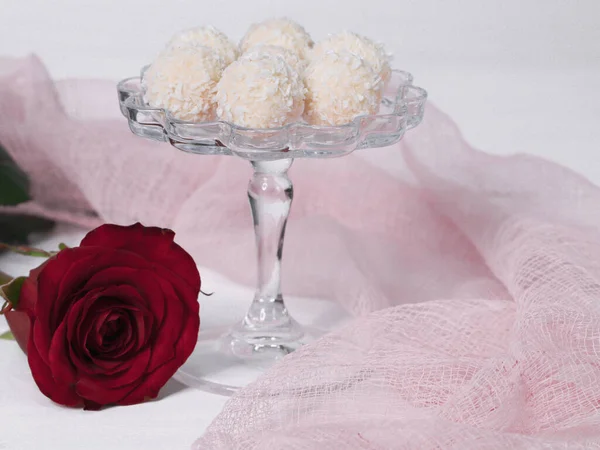 Raffaello candies in a candy bowl and a red rose with pink gauze on the table, close-up side view.