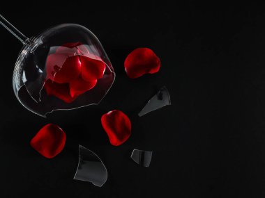 Broken glass and rose petals with fringes lie on the left against a black background with space for text on the right, top view.