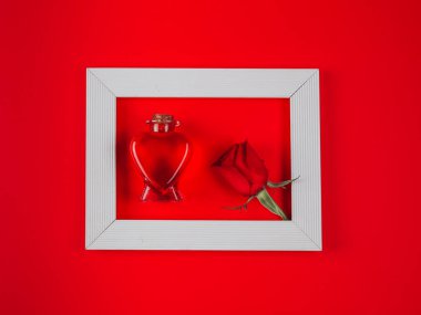 Heart and rose in a white wooden frame lie in the middle on a red background, top view close-up.