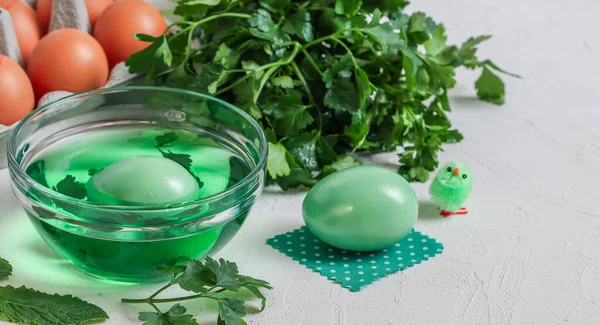 Two eggs, herbs and natural paint in a bowl with Easter chicken on a light background with a place for text on the right, close-up side view.