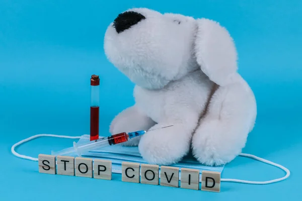 Syringe vaccine dog toy and the word stop covid on a blue background, close-up side view.