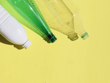 Sarı arka planda üç farklı plastik şişe, aşağıdan mesaj için bir yer, yakın çekim üst görünüm..