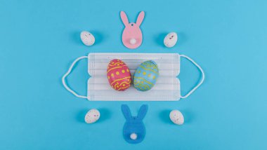 Tavşanlı ve maskeli Paskalya yumurtaları mavi bir arka planda, yakın plan bir üst görünümde duruyor..