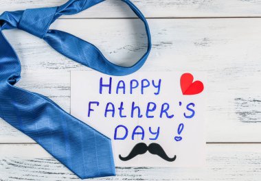 Babalar günü kartlı mavi kravat ve kalbi olan kağıt bıyıklı beyaz eski püskü ahşap bir masa, yakın çekim manzaralı..