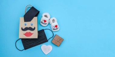 Bir alışveriş çantası, maske ve hediye edilmiş çocuk ayakkabısı sol tarafta mavi bir arka planda yatıyor, sağda yazı için bir yer, yakın çekim üst görünümü var..