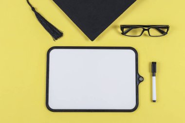 Beyaz tahta, gözlük, keçeli kalem ve mezuniyet şapkası sarı arkaplanda metin için yer, üst görünüm yakın çekim.