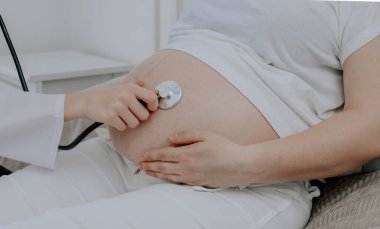 Doktor, koğuştaki hamile bir kadının karnına steteskopla yakından bakıyor..