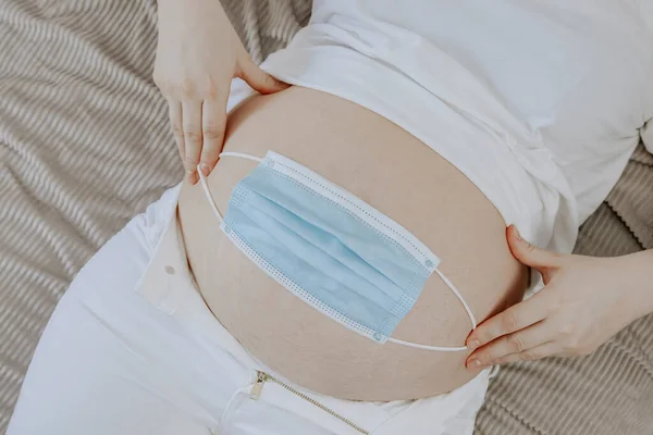 妊娠中の女性は腹の上に医療マスクを保持しているベッドの上に横たわっているビュー クローズアップ — ストック写真