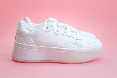 Beyaz spor ayakkabılar pembe arka planda, yakın çekimde ortada yatar..