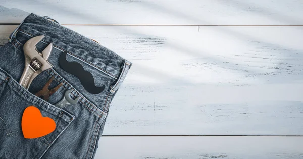 Old construction tools lie in a jeans pocket on the left on a white wooden table with space for text on the right, top view close-up.