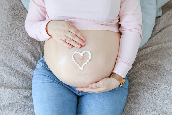 一个孕妇用奶油做的心脏紧紧抓住她的腹部 这是特写 — 图库照片