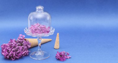 Külahta leylak çiçekleri ve bir pasta tabağında solda mavi bir arkaplan üzerinde uzanıyor. Sağ tarafta yazı için yer var, yakın plan yan görünümü için..