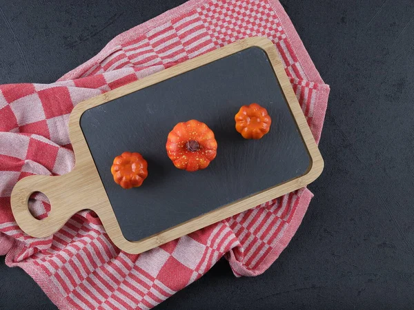 A black board and three decorative pumpkins with a kitchen napkin lie on a black background, a close-up top view.