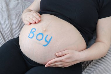 Hamile bir kadın göbeğini boyadan yapılmış bir yazıyla tutar: çocuk, yan plan yakın çekim.