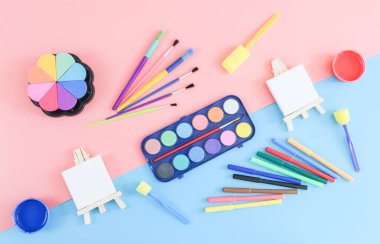 Bir dizi aksesuar: iki sehpa, suluboya boya, akrilik, fırça, sünger, pullar pembe ve mavi arka planda yer alır. Okula dönüş kavramı.