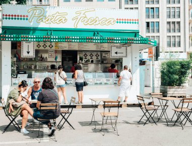 Lüksemburg Şehri, Lüksemburg: 22 Temmuz 2021: Avrupalı görünümlü insanlar şehir merkezinde kuyrukta bekleyen insanlar ve modern binaların bulunduğu bir şehir manzarası olan bir mobil mağazanın yanında yemek yiyorlar. Yatay görüntü, kenar görünüm, yakın plan.