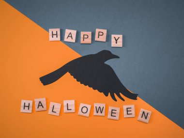 Kağıt karga ve yazılı tahta küpler: Mutlu cadılar bayramı gri-turuncu arka planda, yakın planda yatar. Tebrik kartı kavramı.