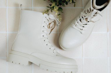 A beautiful view of one pair of fashionable stylish womens classic shoes of cream color with rough soles and laces lie on the tiled floor with a flower in a pot, flat lay very close-up. Concept of womens shoes, fashion collection.