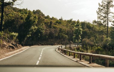 Güneşli bir sonbahar gününde, bir adanın orman dağlarında keskin bir sağ dönüş yapan asfalt yoldaki bir arabadan güzel bir manzara. Zaman yolculuğu kavramı, dağ yolları.