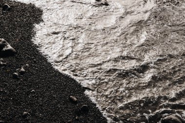 Tenerife 'de sonbahar günbatımında, siyah bir volkanik plajın kıyısındaki sakin ve rahatlatıcı bir dalganın güzel manzarası, yukarıdan yakın çekim. Doğanın arka planlarını ve duvar kağıtlarını kavra.