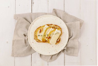 Bir tane armut, peynir, fındık, bal ve mısır gevreği ekmeğindeki bir dal biberiyeli sandviç ortada bir peçetenin üzerinde duran beyaz ahşap bir masanın üzerinde, orta ölçekli tarla derinliğinde bir atış. Sağlıklı gıda konsepti.