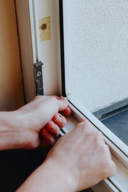 Pencerenin sol alt köşesine beyaz kauçuk yalıtım yapıştıran genç bir beyaz adamın portresi ikinci kattaki bir odanın pervazına yakın, yukarıdan çok yakın bir yan görüntü. Tamir ve yalıtım konsepti