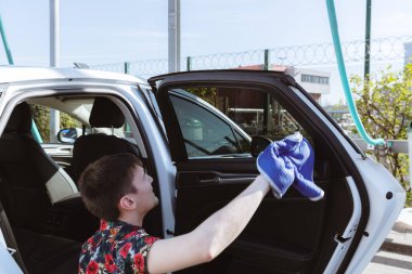 Genç bir beyaz adamın portresi dikkatle inceleniyor ve mavi bir bez parçasıyla güneşli bir bahar günü araba yıkama yerinde arabanın kapısının içinden bardağı yıkıyor. Araba yıkamayı, çalışan insanları kavramsallaştır..