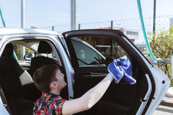 Genç bir beyaz adamın portresi dikkatle inceleniyor ve mavi bir bez parçasıyla güneşli bir bahar günü araba yıkama yerinde arabanın kapısının içinden bardağı yıkıyor. Araba yıkamayı, çalışan insanları kavramsallaştır..