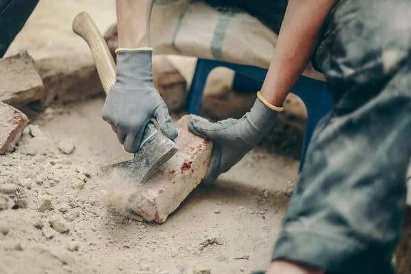 Siyah iş elbiseli beyaz bir genç adam sağdaki küçük bir sandalyeye oturur ve toprak, enkaz ve eski çimentoyu balta ile temizler. İnşaat konsepti..