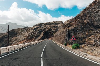 Güneşli bir sonbahar gününde güneşli bir adada bulutlu bir gökyüzü olan, asfalt bir yolda bir arabanın güzel yatay manzarası, yakın çekim. Kavram: yol gezisi, dağ yolları.