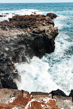 Atlantik Okyanusu 'ndaki bir adanın kuzey kıyısında bir dalganın çarptığı ve parçalandığı kayalık bir volkanik kıyı şeridinin güzel dikey görüntüsü, yukarıdan yakından izleniyor. Güzel doğal altyapı ve duvar kağıtları kavramı.